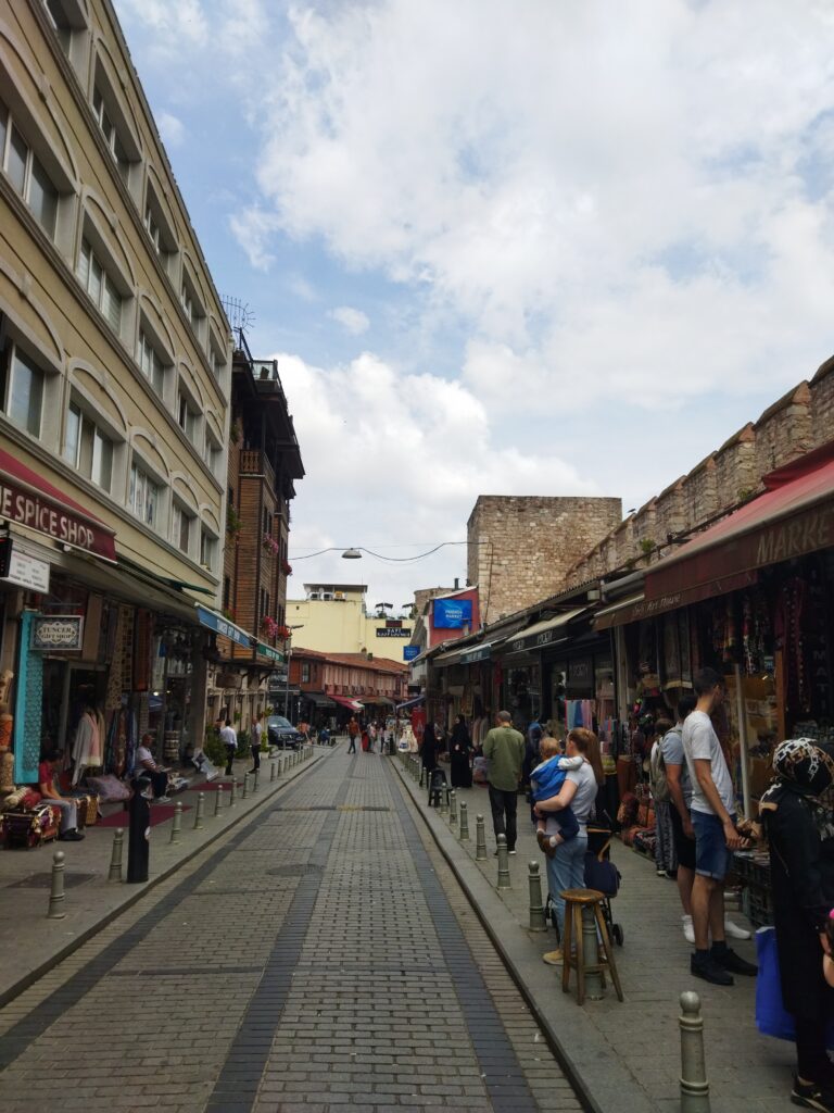 A lively street near the Grand Bazaar in Istanbul, lined with traditional shops and local people walking along a cobblestone road