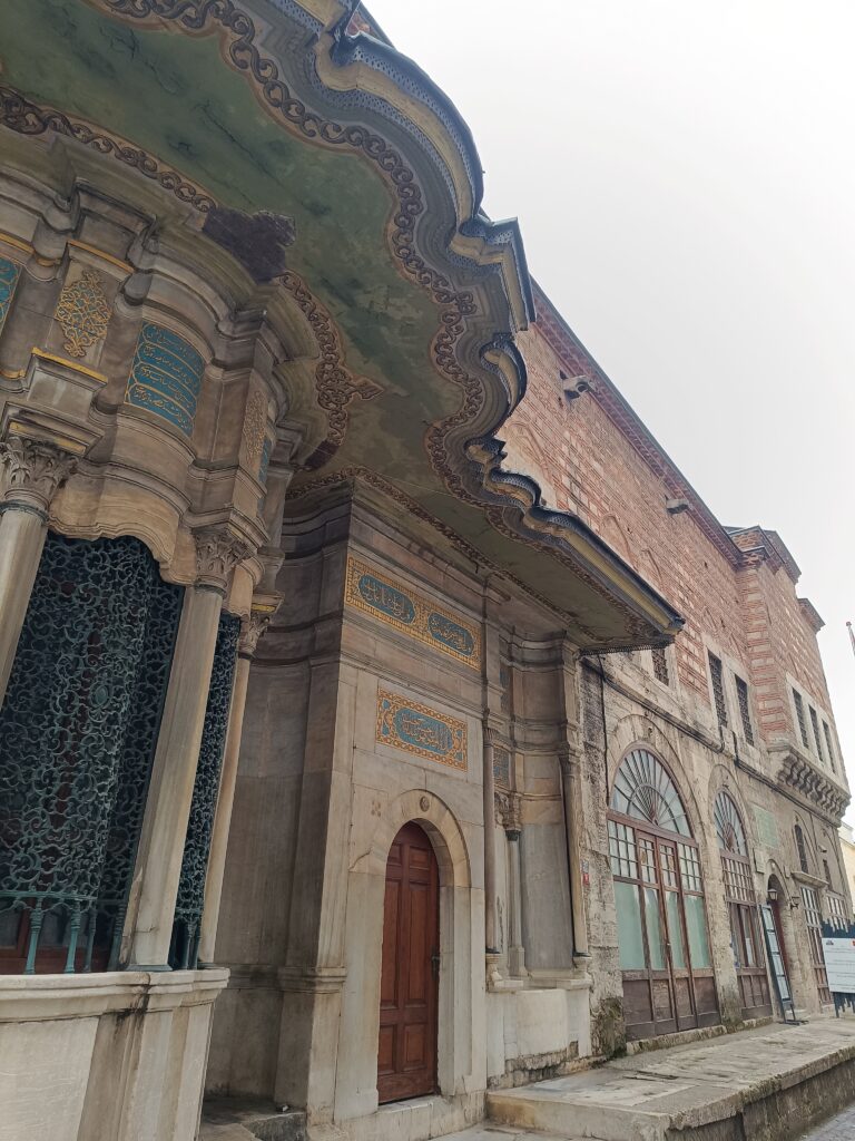 An ornate Ottoman-era building facade in Istanbul with decorative arches, stone columns, and Arabic calligraphy panels